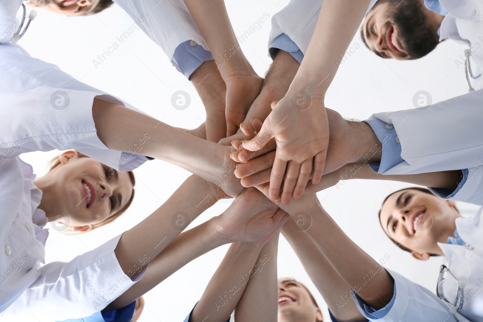 Photo of Team of medical doctors putting hands together on white background, closeup. Unity concept