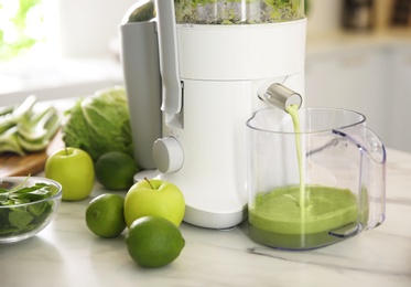 Photo of Modern juicer and fresh fruits on table in kitchen