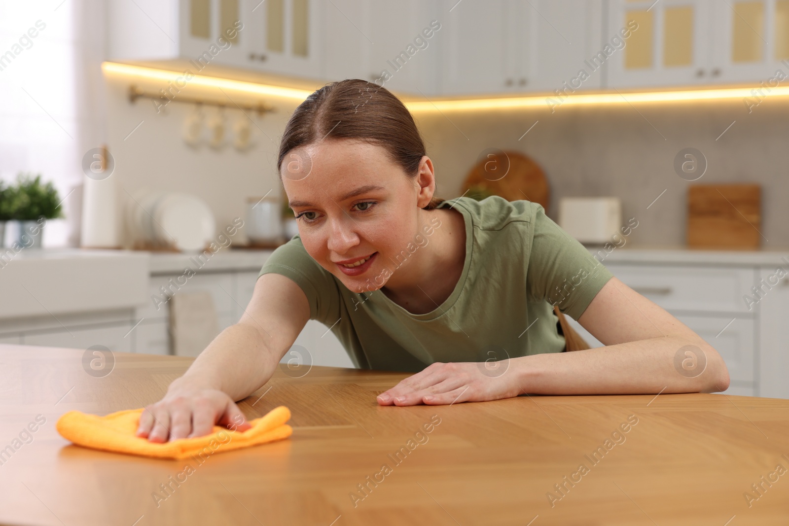 Photo of Woman with microfiber cloth cleaning wooden table in kitchen