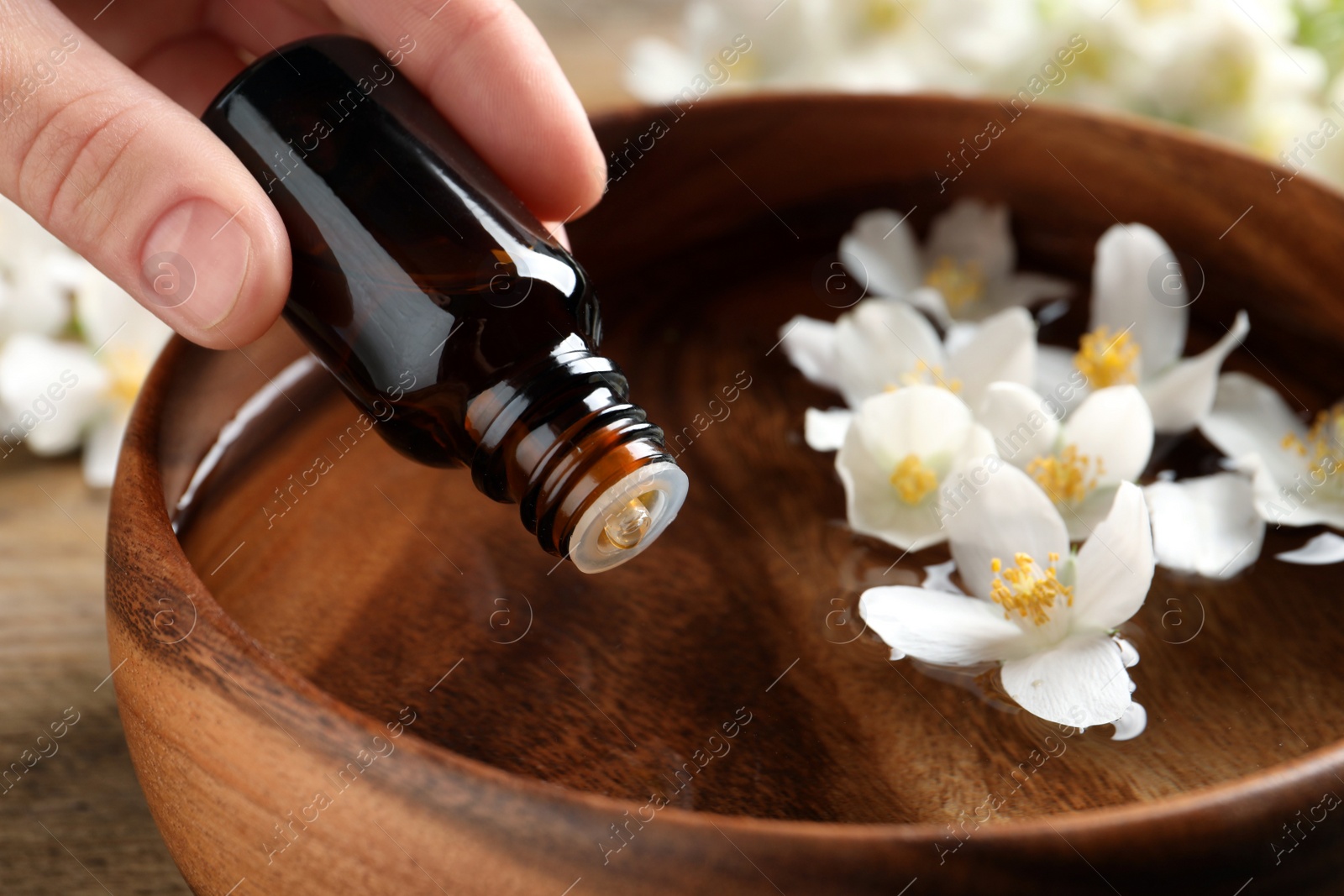 Photo of Woman dripping jasmine essential oil into wooden bowl on table, closeup