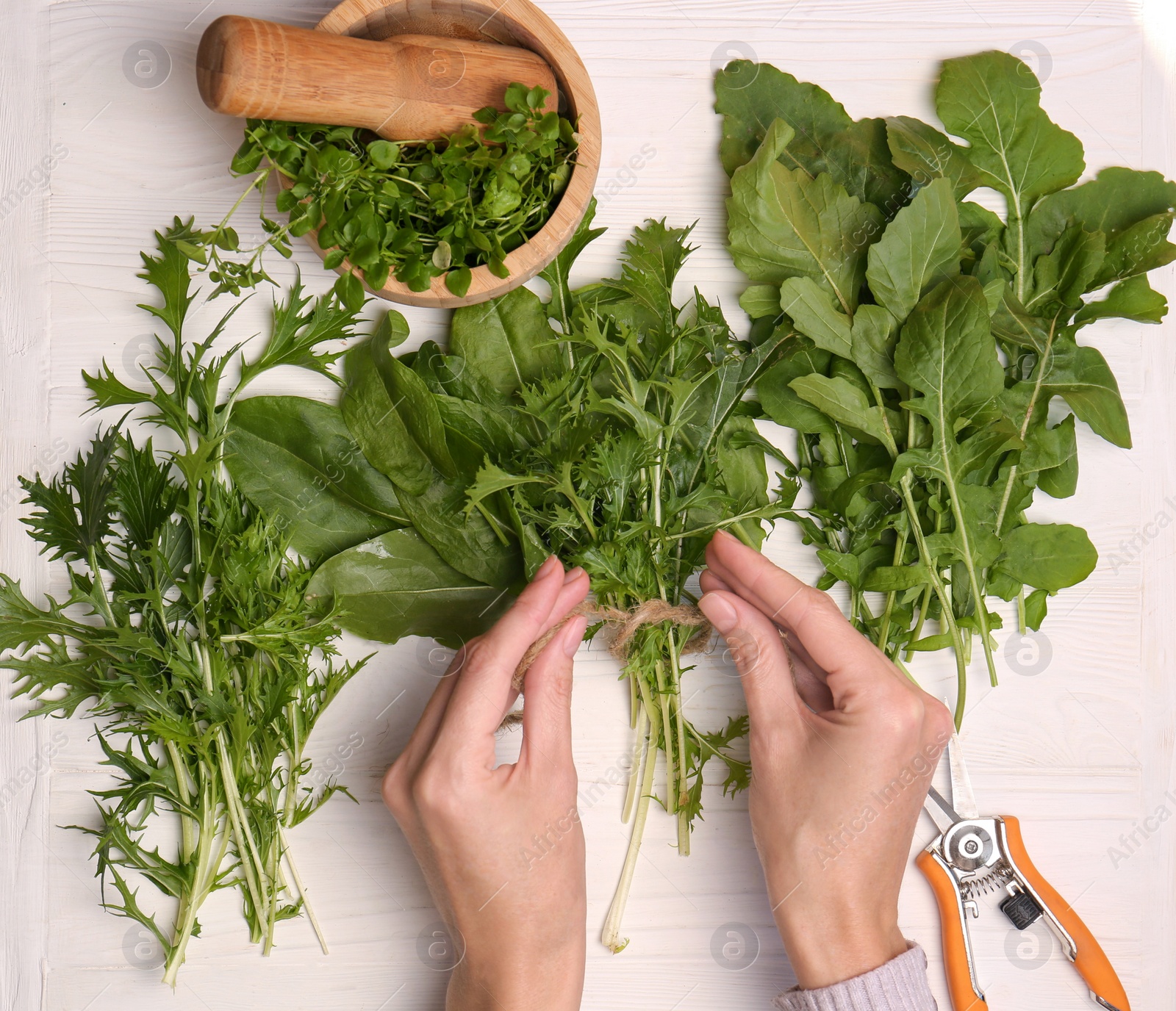 Photo of Woman tying bunch of fresh green leaves with twine at white wooden table, top view