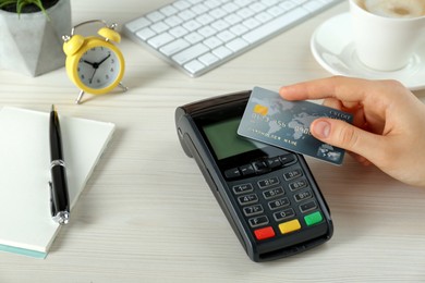 Woman with credit card using modern payment terminal at white table, closeup