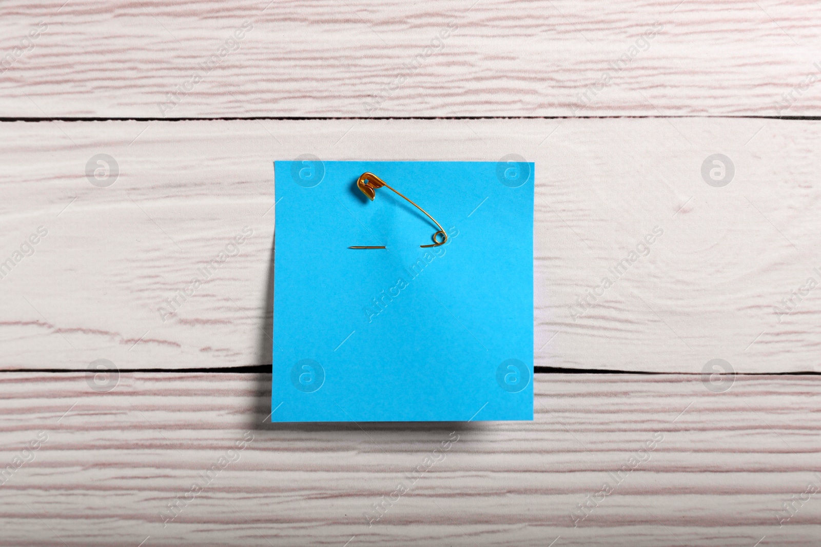 Photo of Blue paper note attached with safety pin to white wooden background, top view