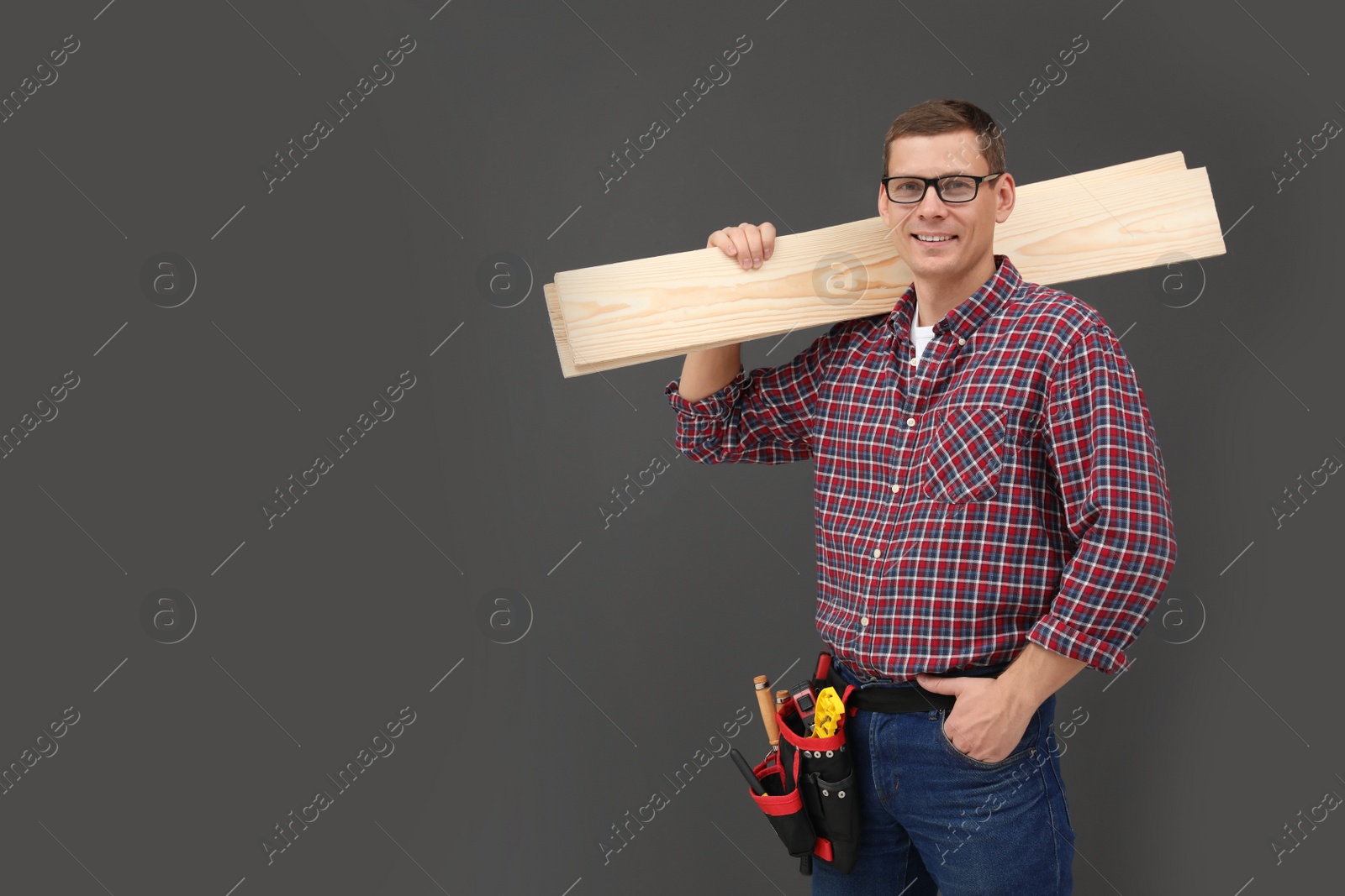 Photo of Handsome carpenter with wooden planks on dark background. Space for text