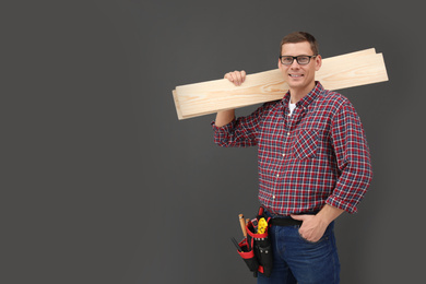 Handsome carpenter with wooden planks on dark background. Space for text