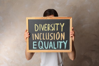 Photo of Woman holding chalkboard with text Diversity Inclusion Equality on beige background