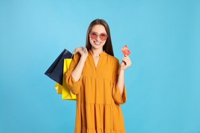 Photo of Happy young woman with shopping bags and credit card on light blue background. Big sale