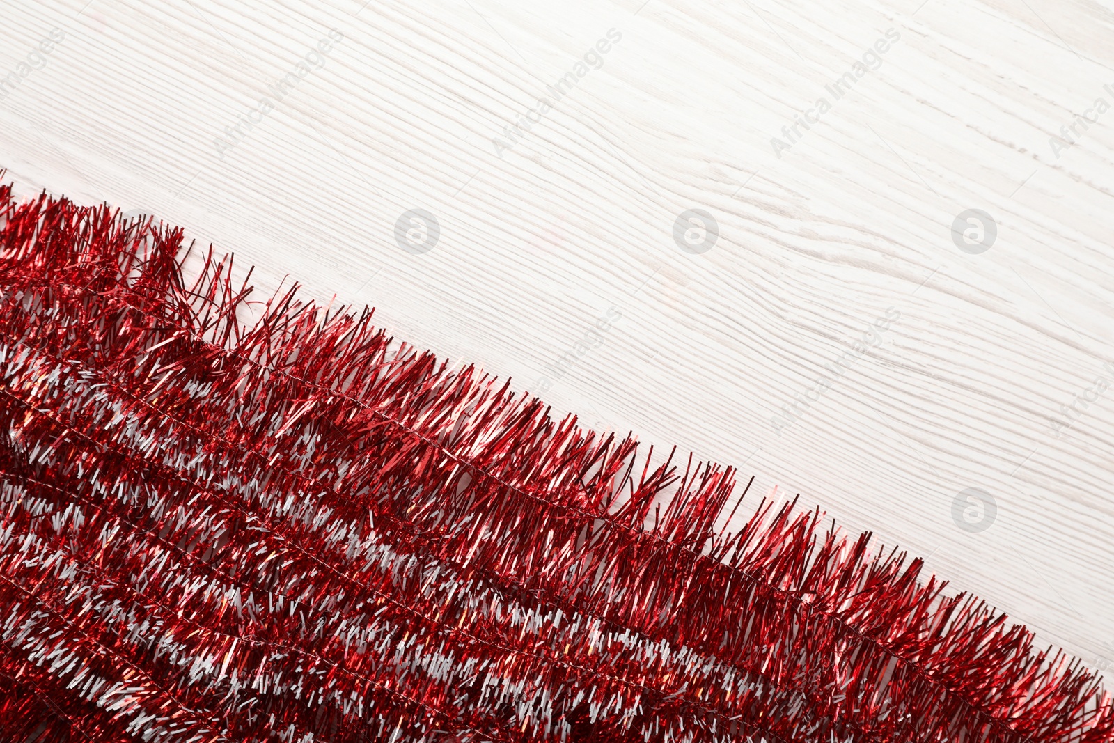 Photo of Shiny red tinsel on white wooden background, flat lay. Space for text