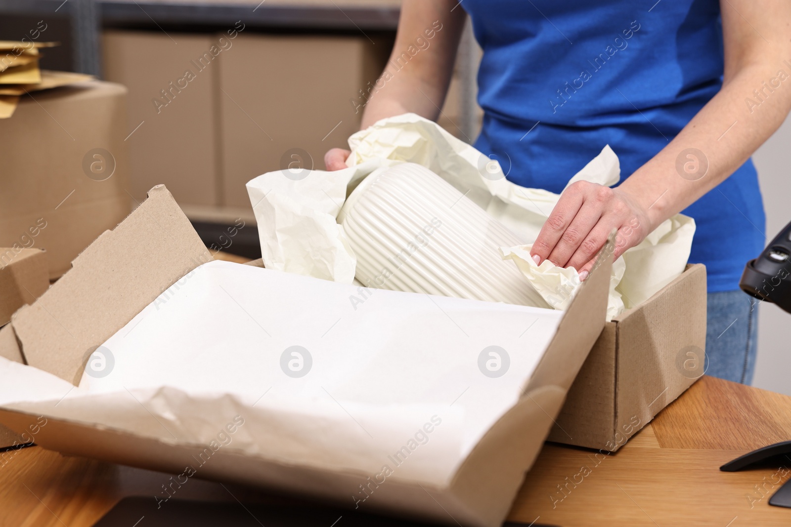 Photo of Post office worker packing parcel at wooden table indoors, closeup