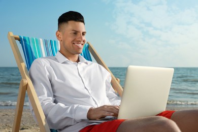 Photo of Happy man working with laptop on beach. Business trip