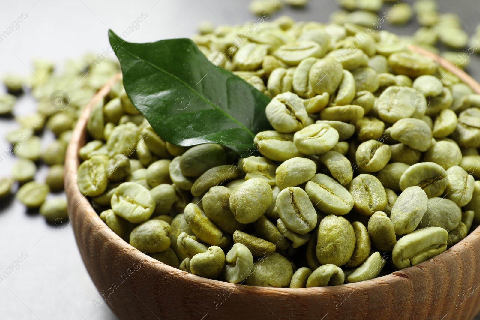 Photo of Green coffee beans and leaf in wooden bowl on table, closeup