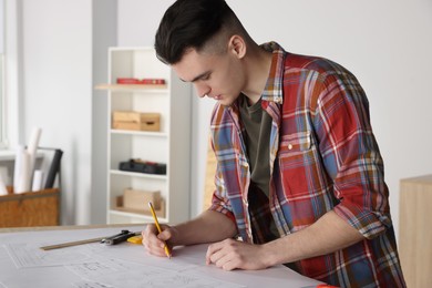 Photo of Young handyman working with blueprints at table in room