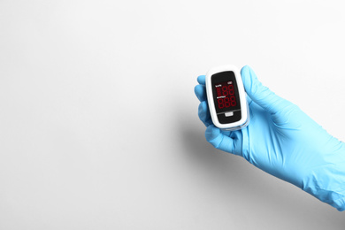 Photo of Doctor in gloves holding fingertip pulse oximeter on white background, closeup. Space for text