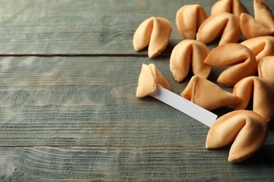 Tasty fortune cookies and paper with prediction on blue wooden table, space for text