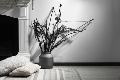 Photo of Black branches with cobweb in vase near fireplace indoors, space for text