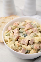 Photo of Tasty Olivier salad with boiled sausage in bowl on white table, closeup