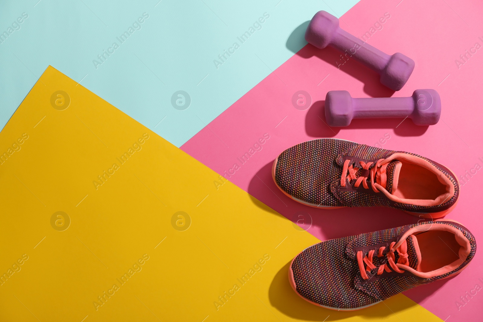 Photo of Dumbbells, sneakers and space for text on color background, flat lay. Physical fitness