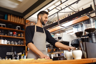 Photo of Smiling barista near coffee machine in cafe, low angle view