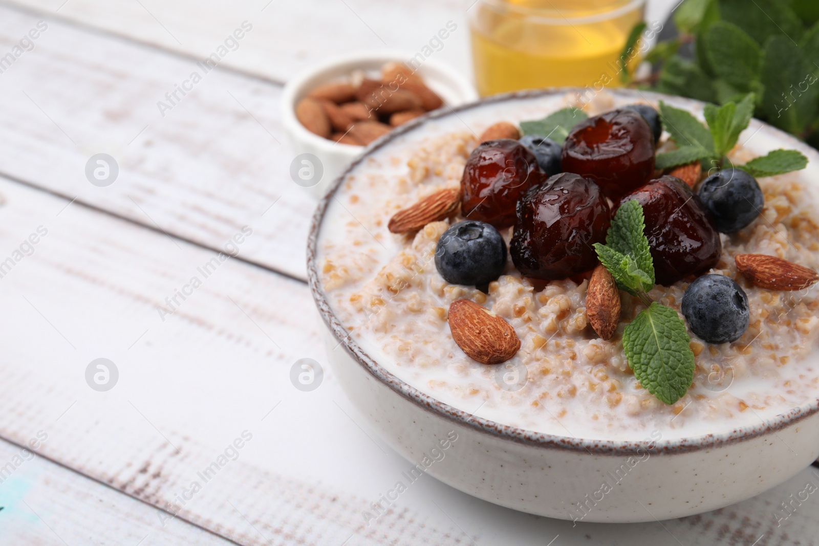 Photo of Tasty wheat porridge with milk, dates, blueberries and almonds in bowl on light wooden table, closeup. Space for text