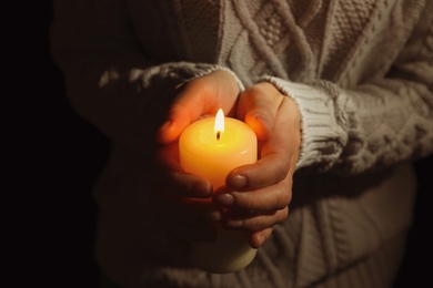 Photo of Young person holding burning candle in darkness, closeup