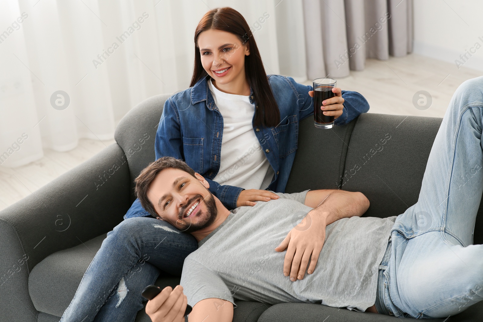 Photo of Happy couple watching show at home. Man changing TV channels with remote control