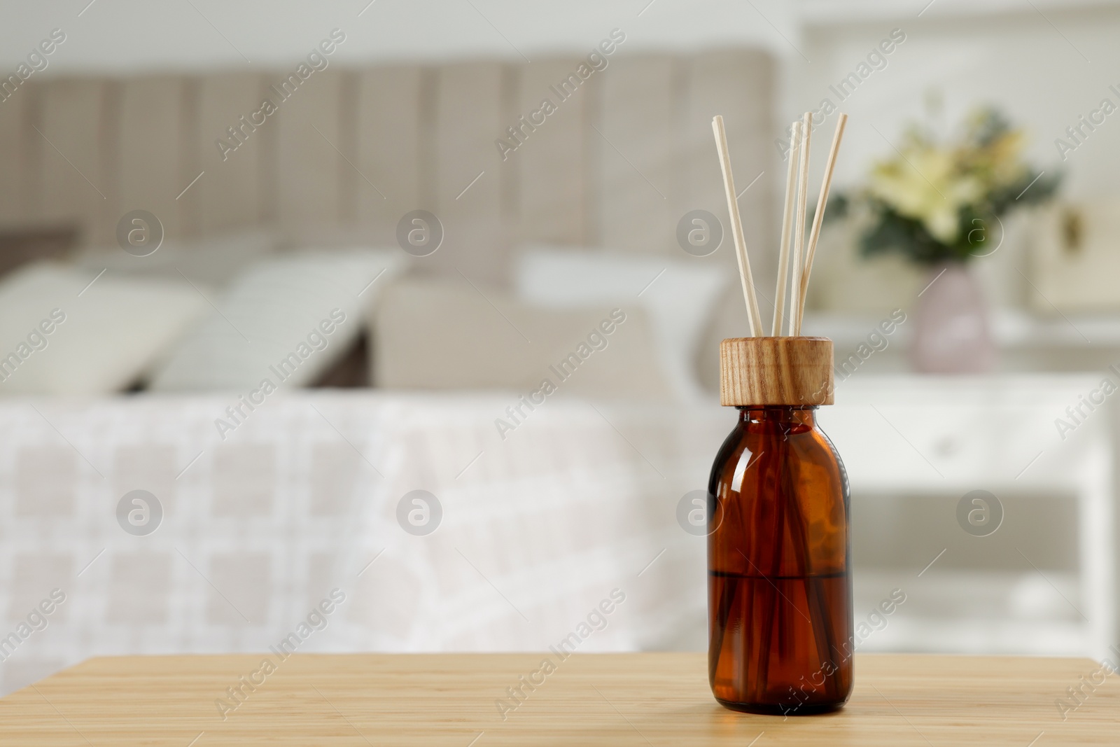 Photo of Aromatic reed air freshener on wooden table in bedroom. Space for text