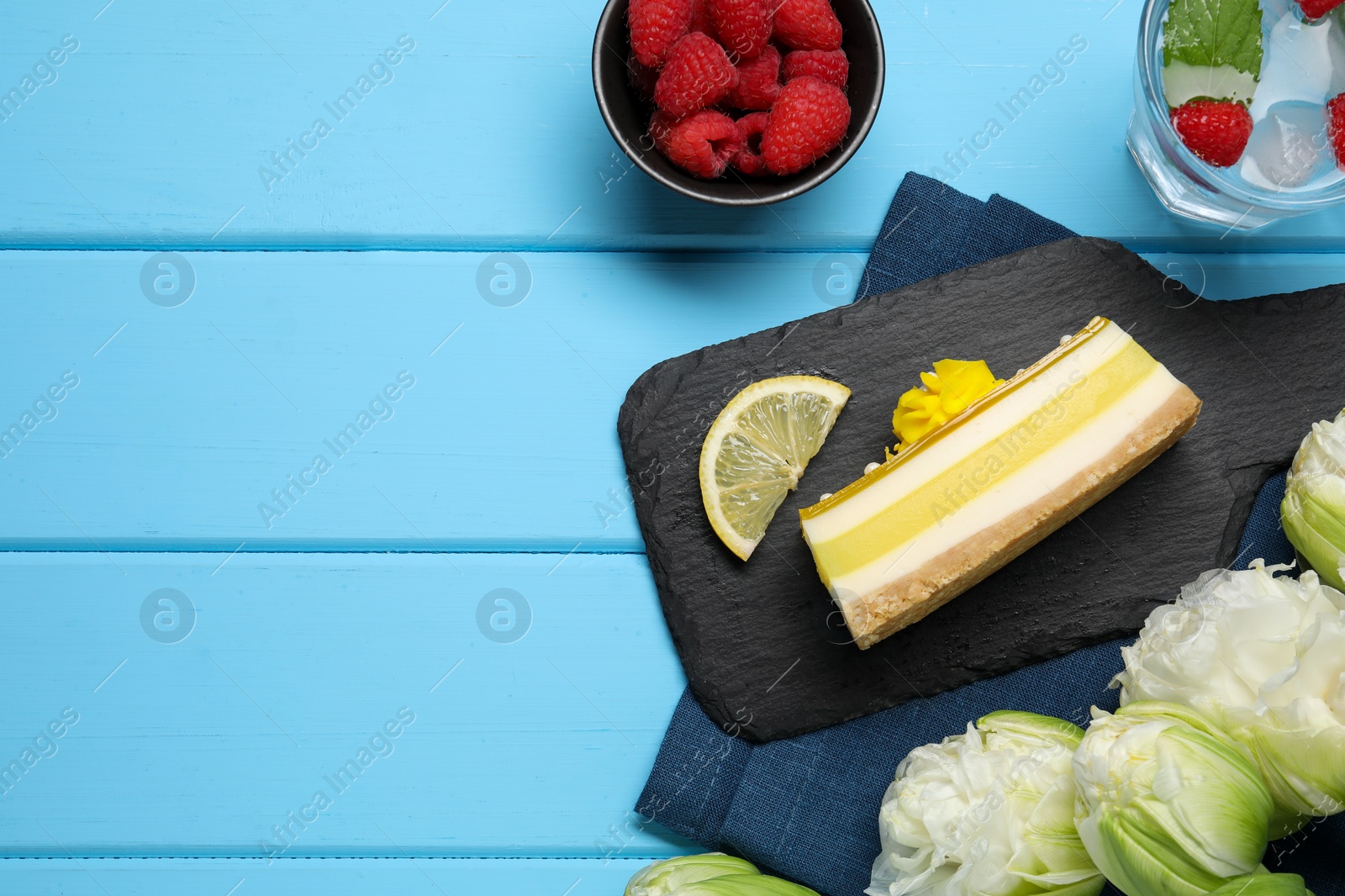 Photo of Delicious cheesecake with lemon, raspberries and peonies on light blue wooden table, flat lay. Space for text