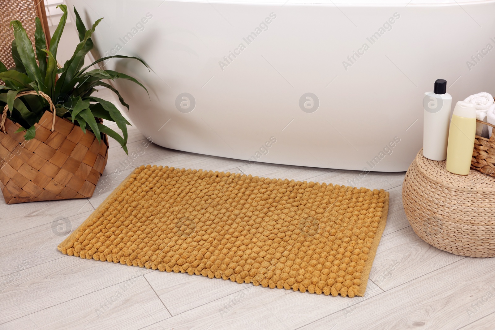 Photo of Soft bath mat, green plant and cosmetic products in bathroom