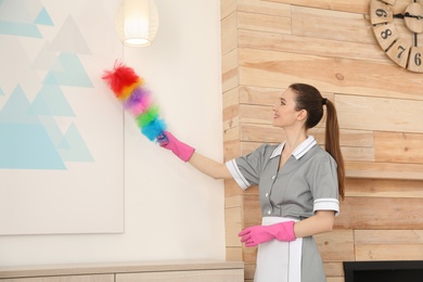 Photo of Young chambermaid wiping dust with brush in hotel room