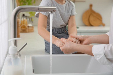 Mother and daughter washing hands with liquid soap together in kitchen, closeup