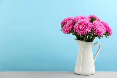 Photo of Beautiful asters in jug on table against light blue background, space for text. Autumn flowers