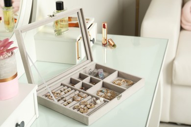 Photo of Elegant jewelry box with beautiful bijouterie, cosmetics and stylish accessories on dressing table in room