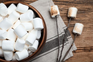 Photo of Sticks with roasted marshmallows on wooden table, flat lay