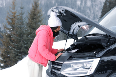 Stressed woman near broken car outdoors on winter day