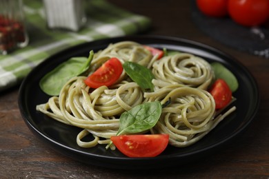 Tasty pasta with spinach, sauce and tomatoes on wooden table, closeup