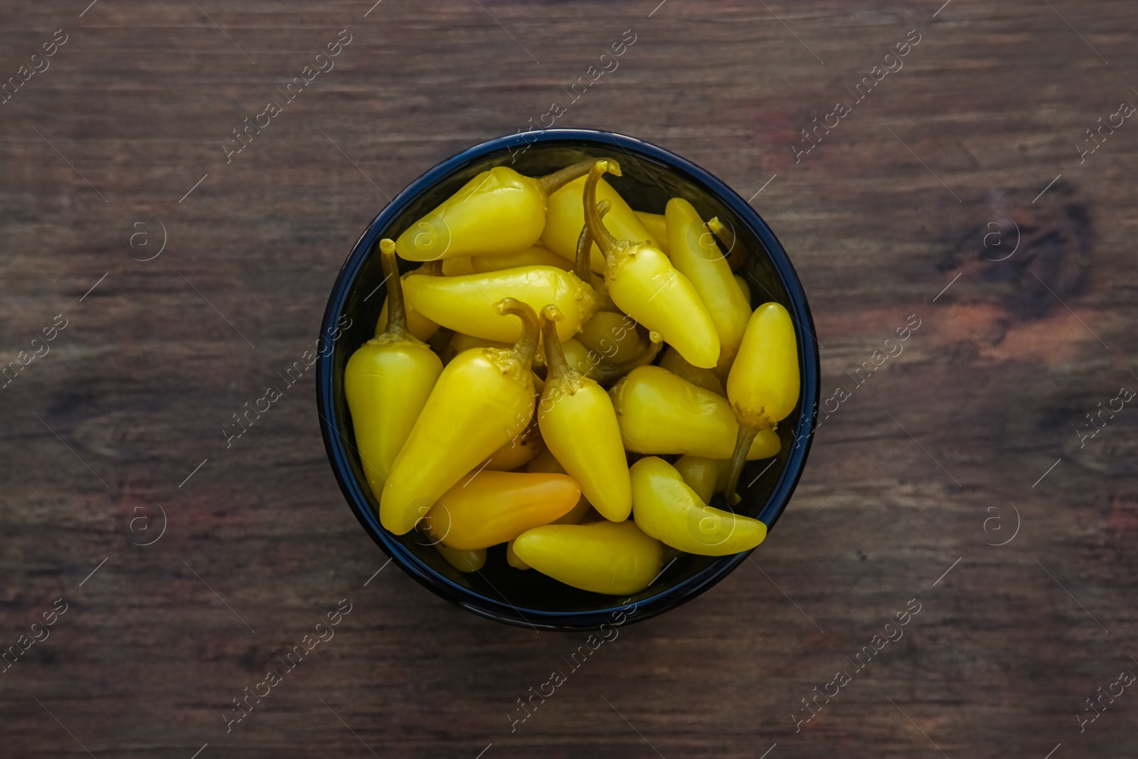 Photo of Bowl of pickled yellow jalapeno peppers on wooden table, top view