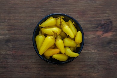 Photo of Bowl of pickled yellow jalapeno peppers on wooden table, top view