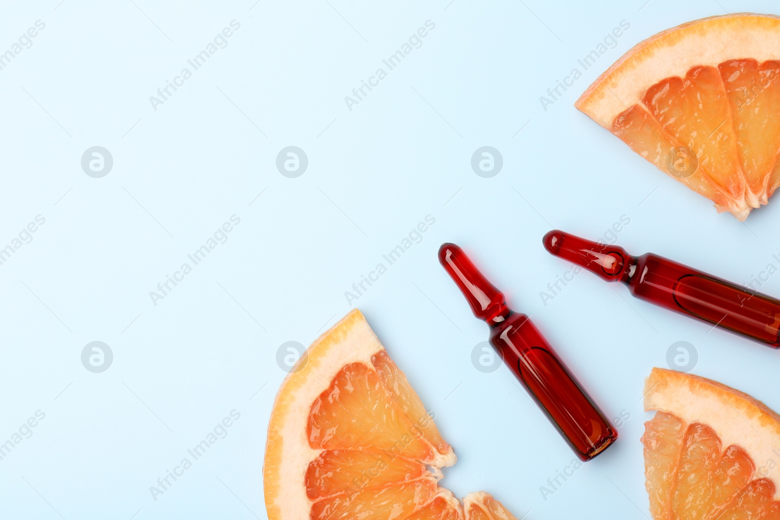 Photo of Skincare ampoules with vitamin C and slices of grapefruit on light blue background, flat lay. Space for text