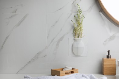 Silicone vase with flowers on white marble wall in stylish bathroom. Space for text