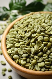 Green coffee beans in wooden bowl on table, closeup