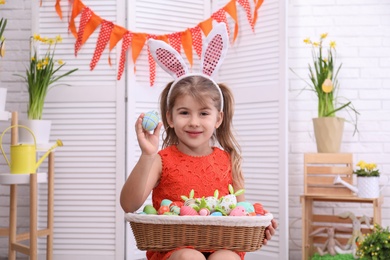 Adorable little girl with bunny ears and basket full of dyed eggs in Easter photo zone