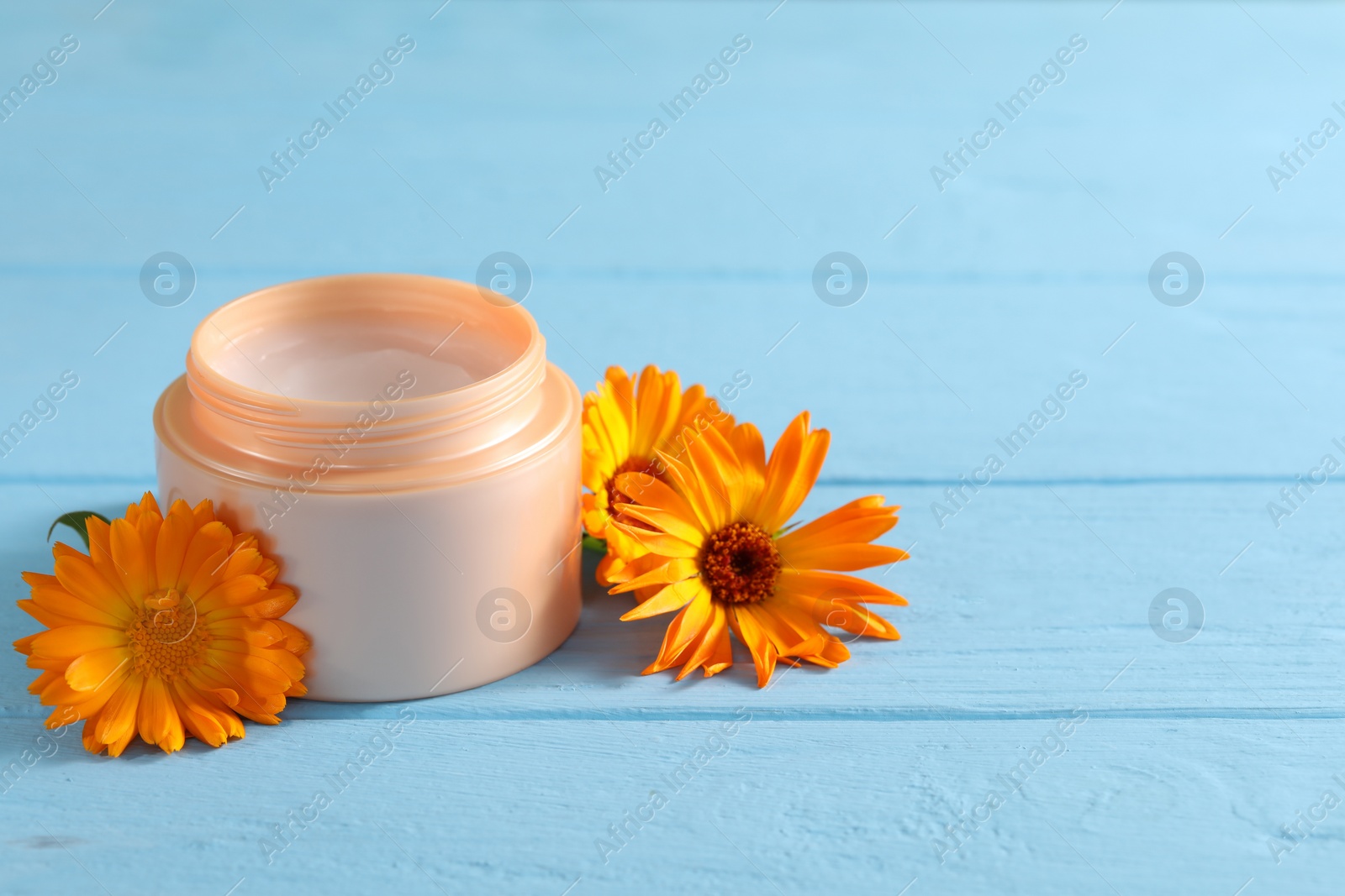 Photo of Jar of cream and beautiful calendula flowers on light blue wooden table, space for text