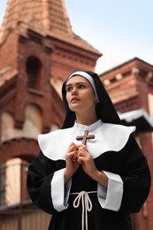 Young nun holding Christian cross near building outdoors