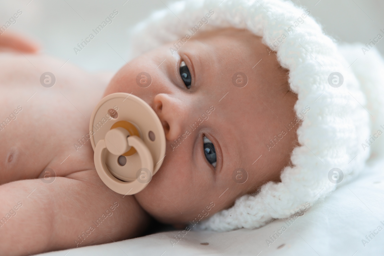 Photo of Cute newborn baby in white knitted hat lying on bed, closeup