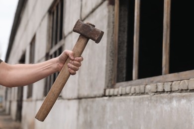 Man with sledgehammer near old building outdoors, closeup. Space for text