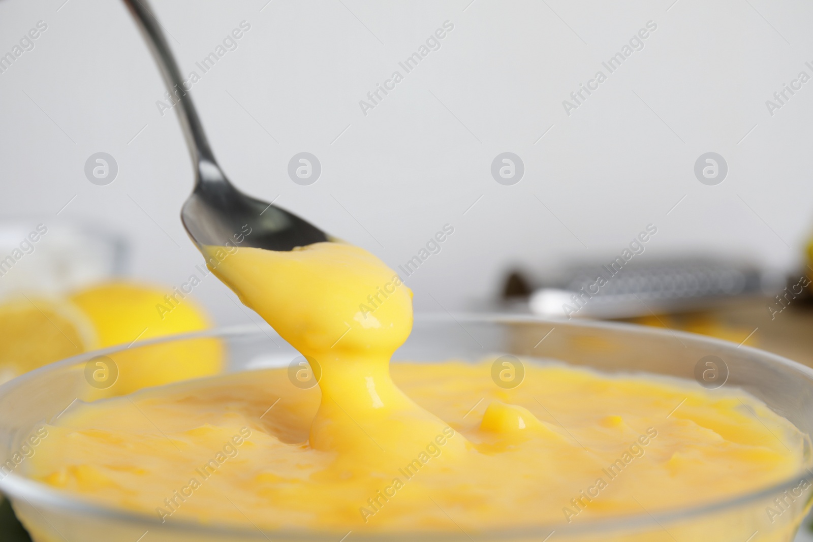 Photo of Spoon with delicious lemon curd above bowl, closeup