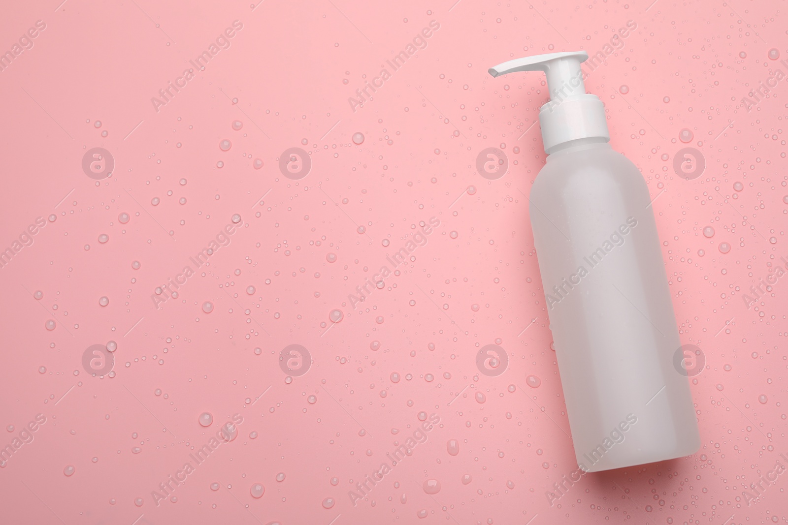 Photo of Wet bottle of face cleansing product on pink background, top view. Space for text