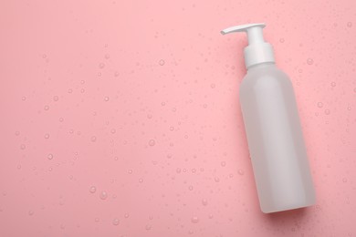 Photo of Wet bottle of face cleansing product on pink background, top view. Space for text