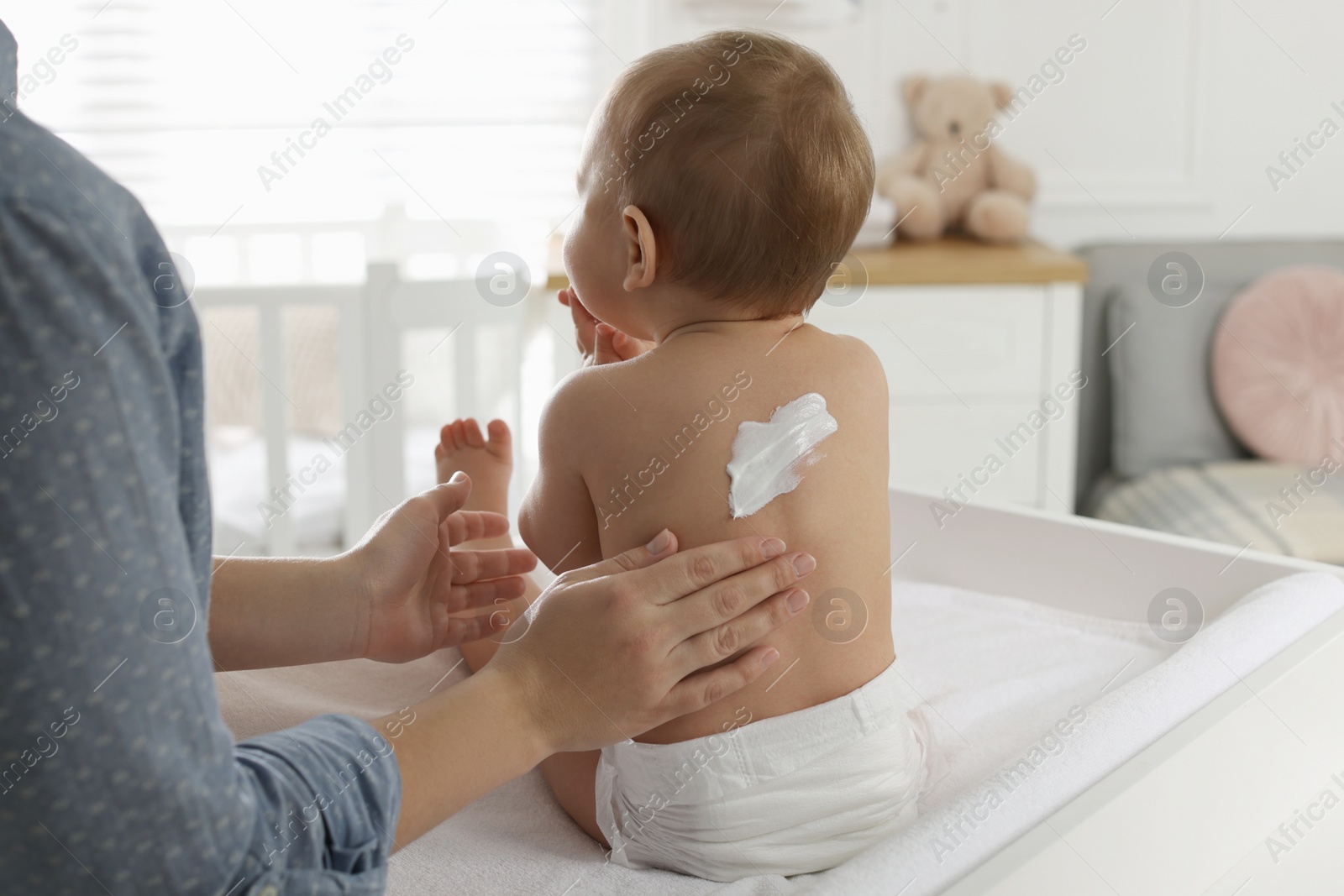 Photo of Mother applying body cream on her little baby at home, closeup