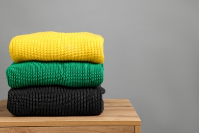 Photo of Stack of knitted sweaters on wooden table against grey background. Space for text